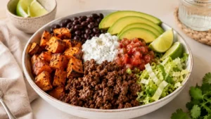 Beef and sweet potato bowl with roasted sweet potatoes, seasoned ground beef, black beans, avocado, salsa, cabbage, lime, and creamy sauce.
