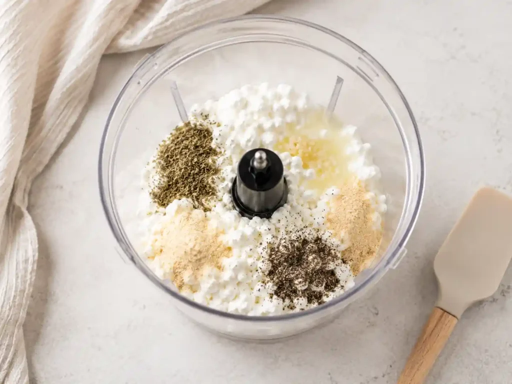 Cottage cheese, lemon juice, herbs, and seasonings being blended into a smooth protein dip.