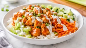 Buffalo chicken rice bowl with saucy chicken, fluffy rice, celery, carrots, green onions, and creamy drizzle.