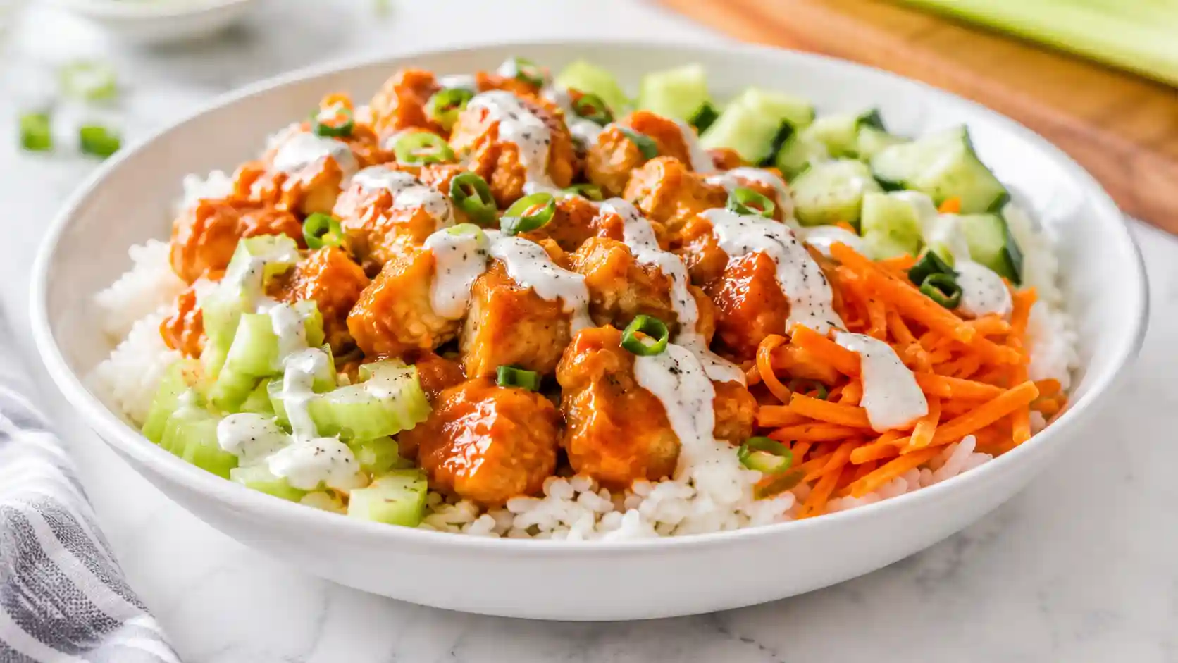 Buffalo chicken rice bowl with saucy chicken, fluffy rice, celery, carrots, green onions, and creamy drizzle.