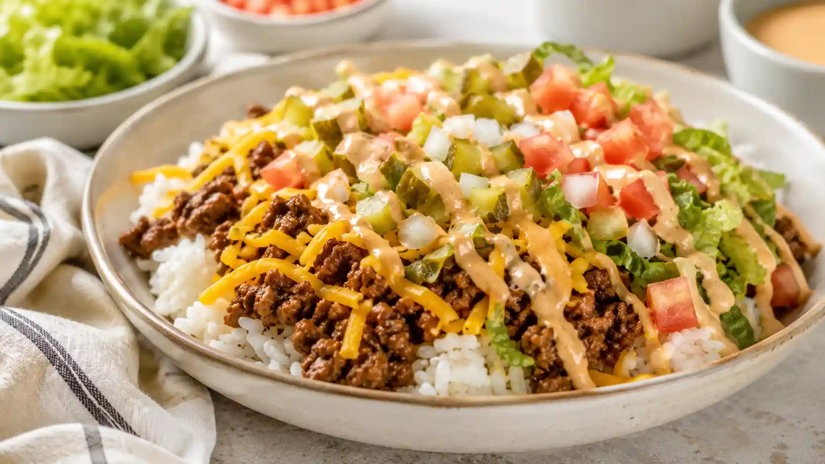 Cheeseburger rice bowl with seasoned ground beef, rice, cheddar, pickles, lettuce, tomato, onion, and burger sauce.