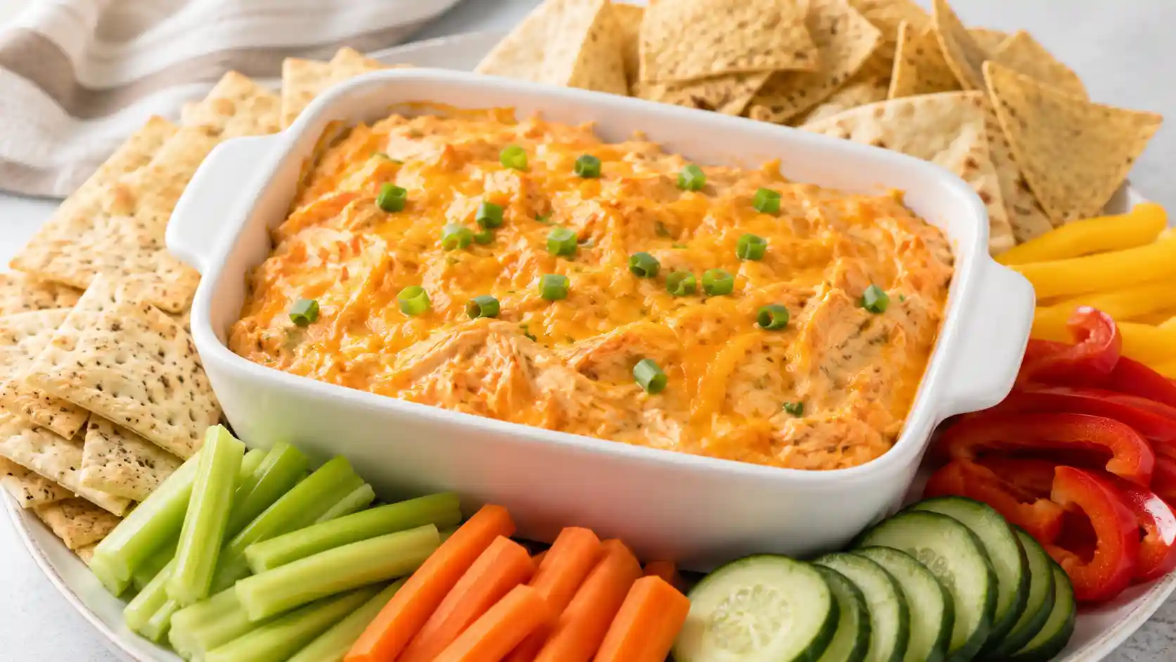 Cottage cheese buffalo chicken dip baked with melted cheese and served with celery, carrots, crackers, and pita chips.
