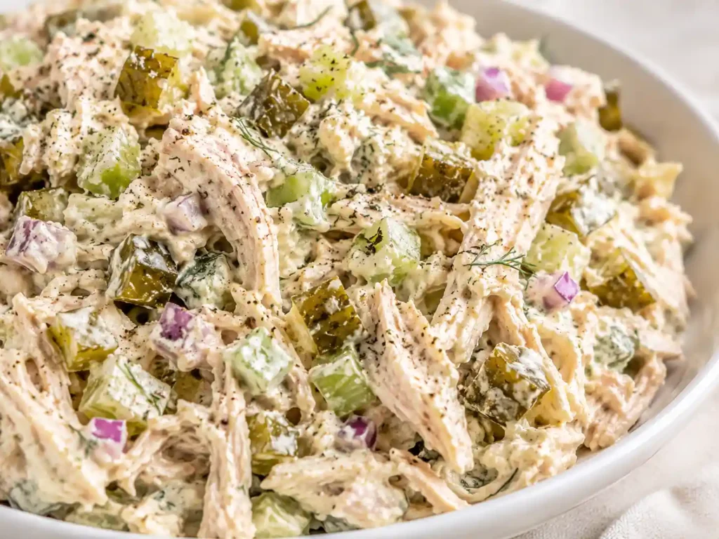 Close-up of creamy dill pickle chicken salad with shredded chicken, chopped pickles, celery, dill, and black pepper.