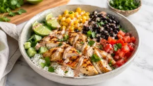 Chicken rice bowl with seasoned chicken, rice, vegetables, sauce, lime, and fresh toppings