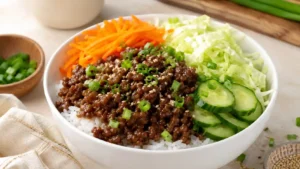 Korean ground beef rice bowl with rice, saucy ground beef, carrots, cabbage, cucumber, green onions, and sesame seeds.