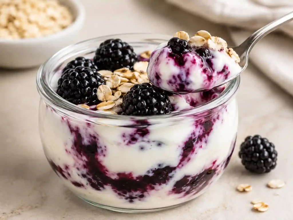 Close-up of creamy blackberry Greek yogurt protein cup with berry swirl and crunchy oat topping.