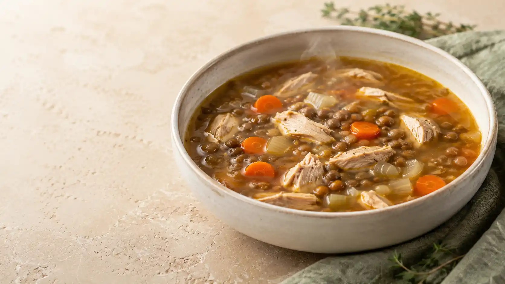 Chicken lentil soup with tender chicken, lentils, carrots, onions, and herbs in a cream bowl