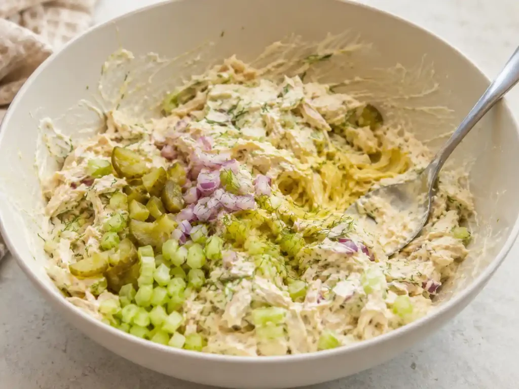 Mixing creamy bread and butter pickle chicken salad in a bowl