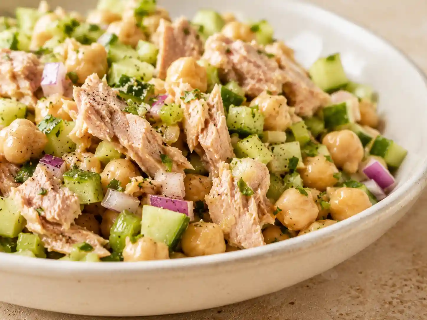 Close-up of tuna chickpea salad showing tuna flakes, whole chickpeas, crisp celery, cucumber, red onion, and light dressing.