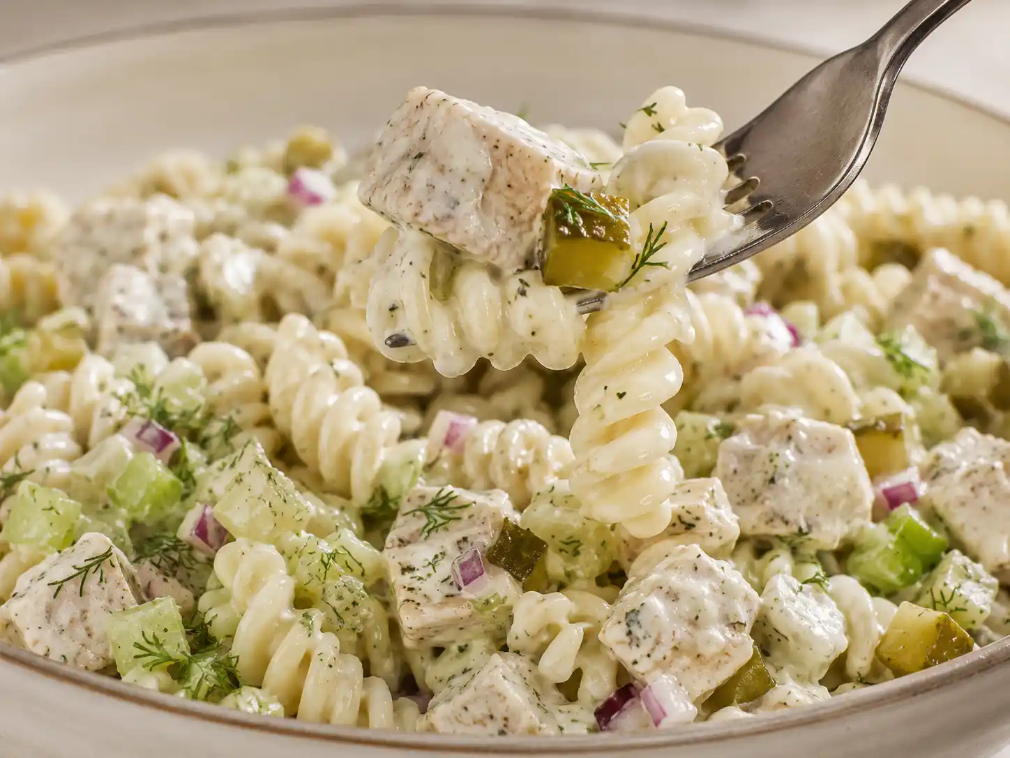 Close-up of creamy rotini, chicken, dill pickles, red onion, celery, and fresh dill