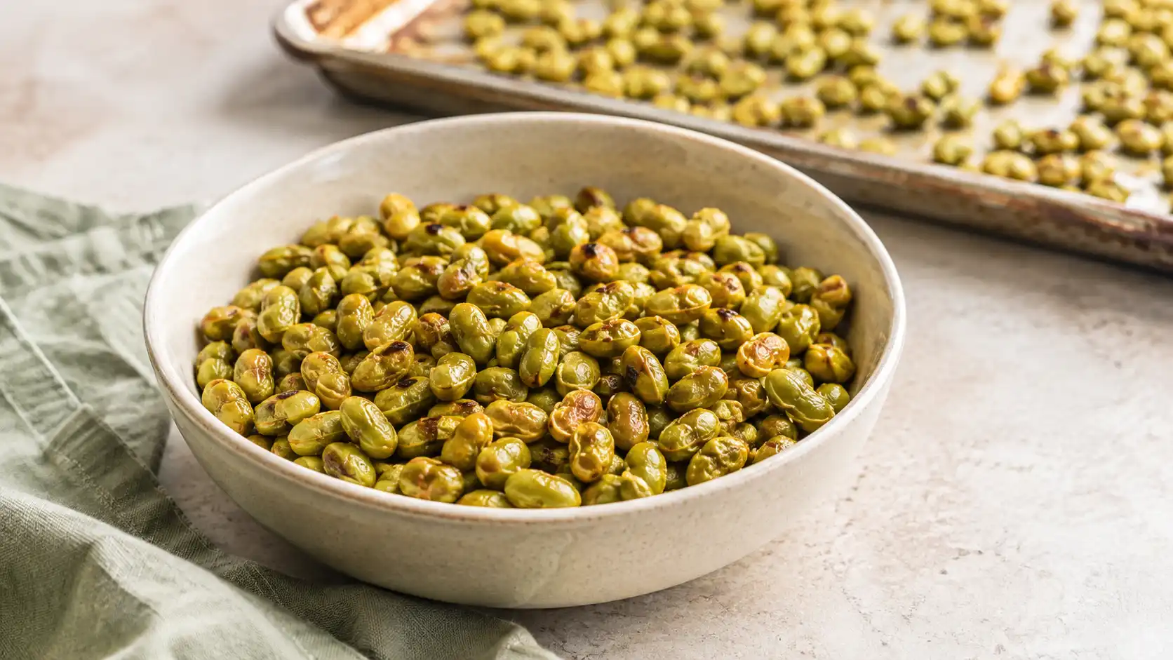 Crispy roasted shelled edamame served in a bowl beside a baking sheet