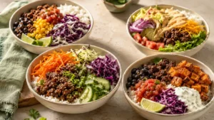 Four ground beef dinner bowls with rice, potatoes, vegetables, beans, pickles, salsa, and creamy sauces